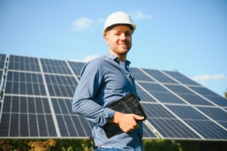 The portrait of a young engineer checks with tablet operation with sun, cleanliness on field of photovoltaic solar panels. Concept: renewable energy, technology, electricity, service, green power