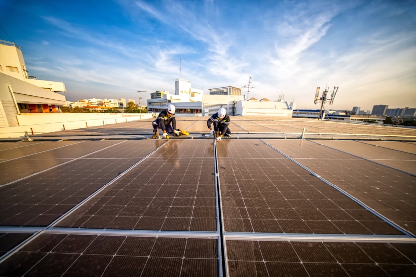 Workers install solar panels on a rooftop in a city during sunset hours