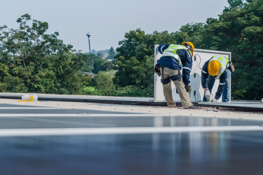 Worker Technicians are working to construct solar panels system on roof. Installing solar photovoltaic panel system. Men technicians carrying photovoltaic solar modules on roof.